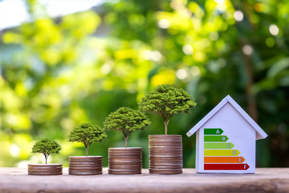 Trees grow on piles of money and energy-saving charts on home models in a residential home energy efficiency assessment concept office.